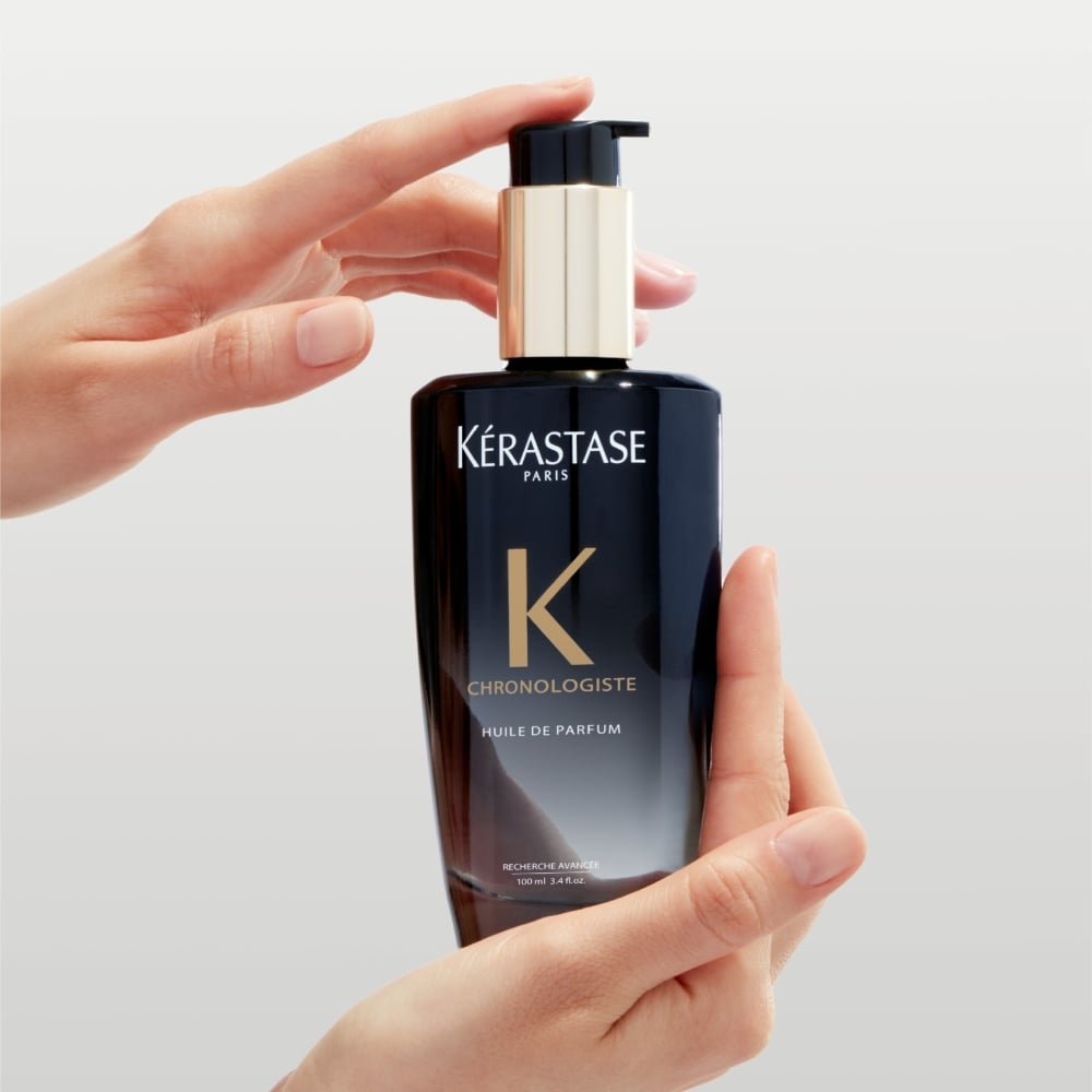  Chronologiste Huile de Parfum, un aceite capilar con una artística mezcla de adictivas fragancias que combinan cedro, magnolia y rosa de té, se sostiene entre dos manos.