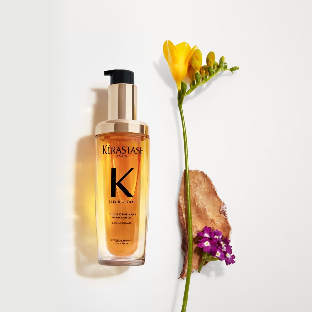 TEl nuevo Elixir Ultime recargable se muestra sobre un fondo gris puro con flores de fresia y heliotropo, y sándalo.
