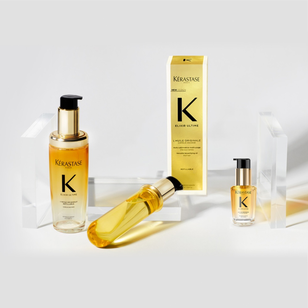 El nuevo aceite capilar Elixir Ultime, su repuesto y el formato de viaje se muestran sobre cubos transparentes en un fondo gris puro.