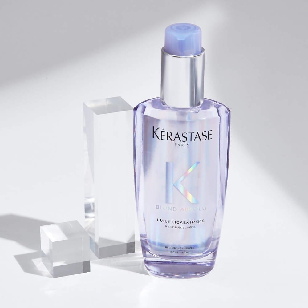  El aceite capilar Huile Cicaextreme se muestra sobre un fondo gris puro con cubos transparentes. El aceite proporciona fuerza y brillo al cabello decolorado y rubio.